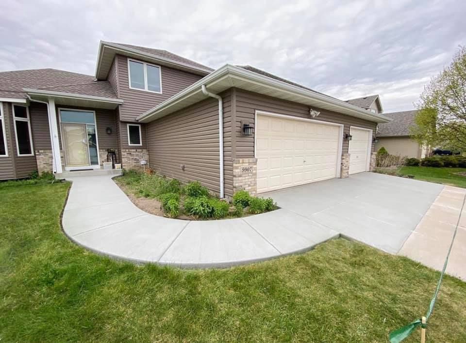 Newly installed concrete driveway and sidewalk in front of a modern two-story house with a two-car garage and landscaped yard in Ramsey, MN.